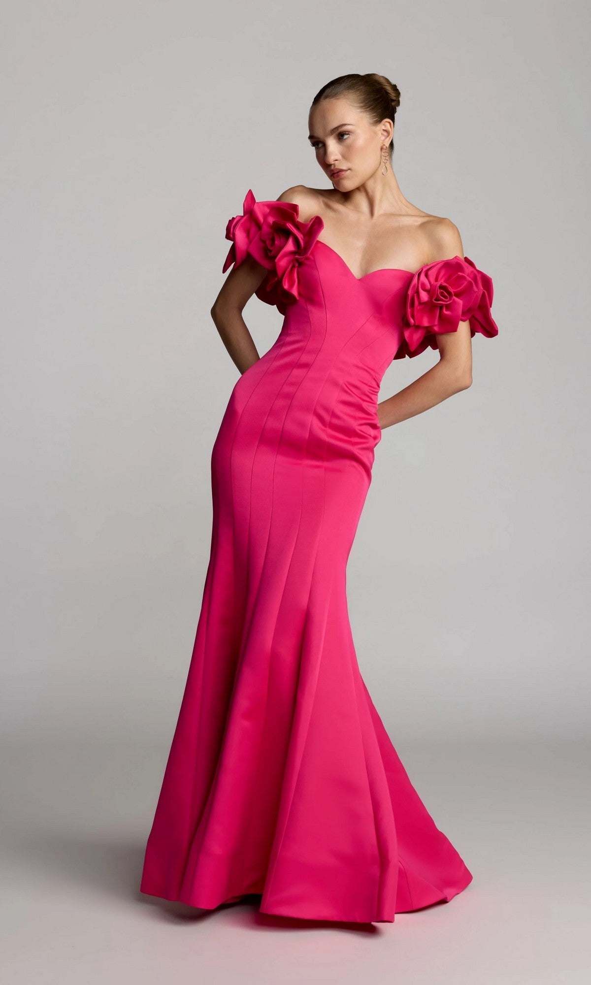A woman wearing the Long Formal Dress: Mac Duggal 21263—a bright pink, off-the-shoulder trumpet gown adorned with large floral sleeve details—poses against a plain light background. Crafted from luxurious satin, this stunning dress brings elegance to any formal occasion.